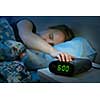 Young woman pressing snooze button on early morning digital alarm clock radio