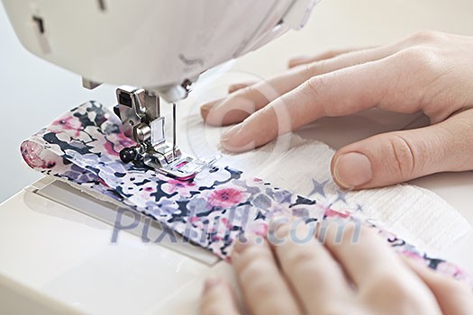 Closeup of hands guiding fabric through sewing machine needle and thread Closeup of hands guiding fabric through sewing machine needle and thread