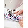 Closeup of hands guiding fabric through sewing machine needle and thread
