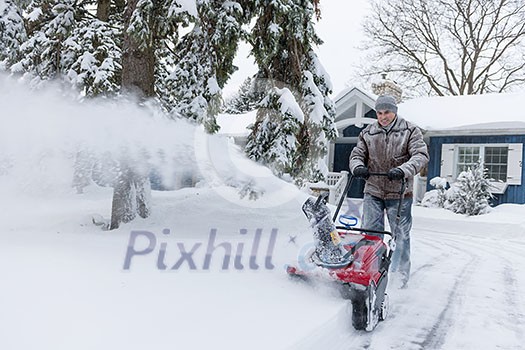 Man using snowblower to clear deep snow on driveway near residential house after heavy snowfall. Man using snowblower to clear deep snow on driveway near residential house after heavy snowfall.