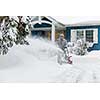 Man using snowblower to clear deep snow on driveway near residential house after heavy snowfall.