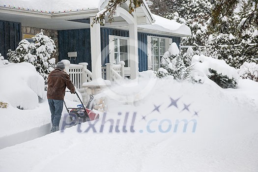 Man using snowblower to clear deep snow on driveway near residential house after heavy snowfall Man using snowblower to clear deep snow on driveway near residential house after heavy snowfall