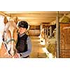 Young female rider with horse inside stable