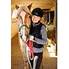Young female rider with horse inside stable