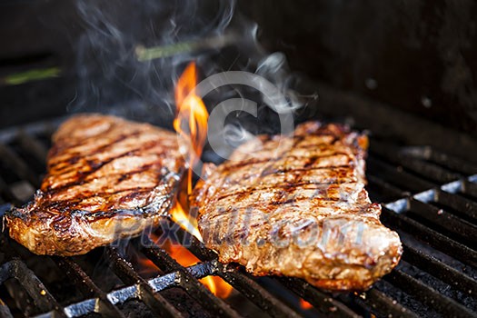 Beef steaks cooking in open flame on barbecue grill Beef steaks cooking in open flame on barbecue grill