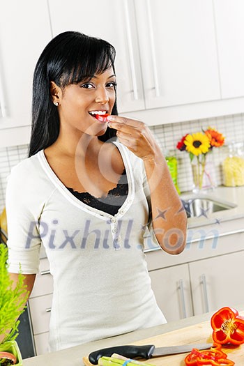 Smiling black woman tasting vegetables in modern kitchen interior Smiling black woman tasting vegetables in modern kitchen interior