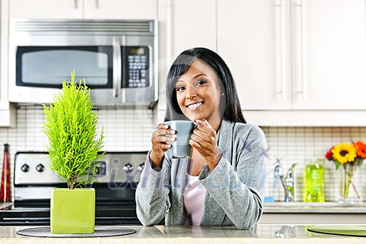 Smiling black woman holding coffee mug in modern kitchen interior Smiling black woman holding coffee mug in modern kitchen interior