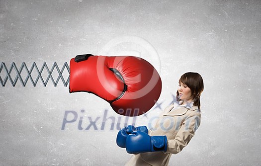 Young businesswoman in blue boxing gloves fighting big red glove on spring Young businesswoman in blue boxing gloves fighting big red glove on spring