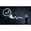 Businesswoman in darkness drawing light bulb with flashlight