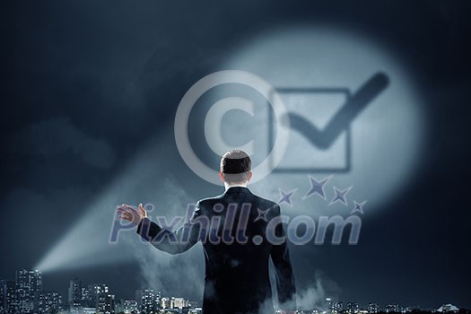 Businessman standing with back and checkbox sign in spotlight Businessman standing with back and checkbox sign in spotlight