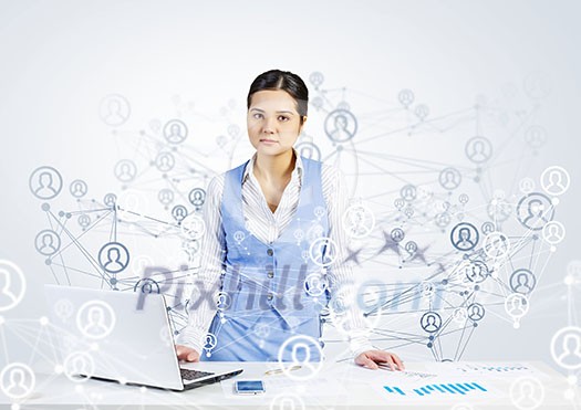 Beautiful young lady at desk working on laptop with social network concept at background Beautiful young lady at desk working on laptop with social network concept at background
