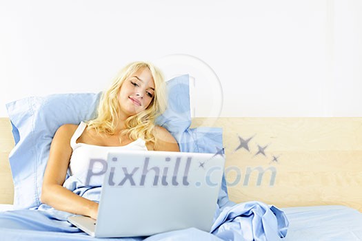 Happy blonde woman using computer at home sitting in bed Happy blonde woman using computer at home sitting in bed