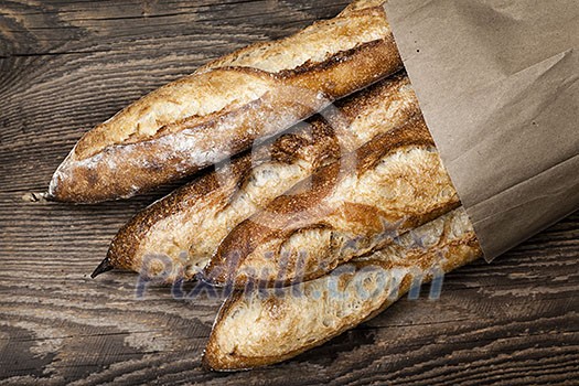 Four baguette bread loaves in paper bag on wooden background Four baguette bread loaves in paper bag on wooden background