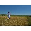 Young woman standing jumping and running  on a wheat field with blue sky in  background at summer day representing healthy life and agriculture concept