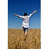 Young woman standing jumping and running  on a wheat field with blue sky in  background at summer day representing healthy life and agriculture concept