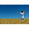 Young woman standing jumping and running  on a wheat field with blue sky in  background at summer day representing healthy life and agriculture concept