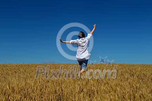 Young woman standing jumping and running on a wheat field with blue sky in background at summer day representing healthy life and agriculture concept Young woman standing jumping and running on a wheat field with blue sky in background at summer day representing healthy life and agriculture concept