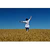 Young woman standing jumping and running  on a wheat field with blue sky in  background at summer day representing healthy life and agriculture concept