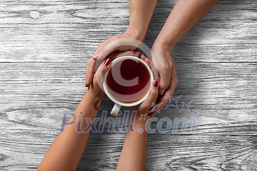 Womans and mens hands holding hot cup of tea on wooden table Womans and mens hands holding hot cup of tea on wooden table