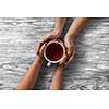 Womans and mens hands holding hot cup of tea on wooden table