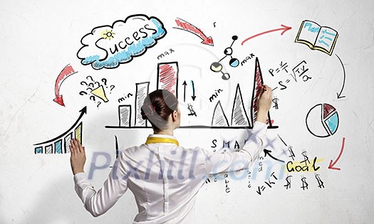 Businesswoman standing with back drawing business ideas on wall Businesswoman standing with back drawing business ideas on wall