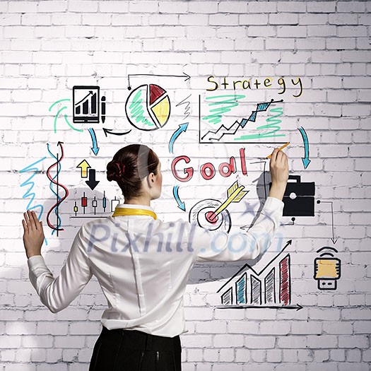 Businesswoman standing with back drawing business ideas on wall Businesswoman standing with back drawing business ideas on wall