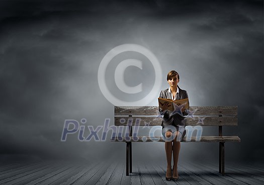 Young smiling businesswoman sitting on bench with book in hands Young smiling businesswoman sitting on bench with book in hands