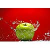 Green apple with water splash on red background
