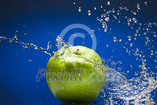 Green apple with water splash on blue background Green apple with water splash on blue background