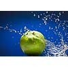 Green apple with water splash on blue background
