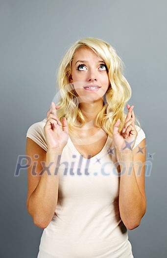 Blonde caucasian woman wishing with fingers crossed on gray background Blonde caucasian woman wishing with fingers crossed on gray background