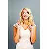 Blonde caucasian woman wishing with fingers crossed on gray background