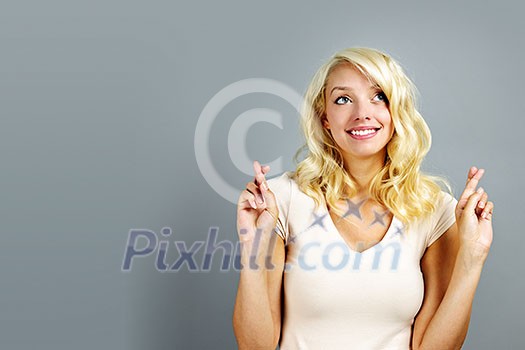 Smiling blonde caucasian woman with fingers crossed on gray background Smiling blonde caucasian woman with fingers crossed on gray background