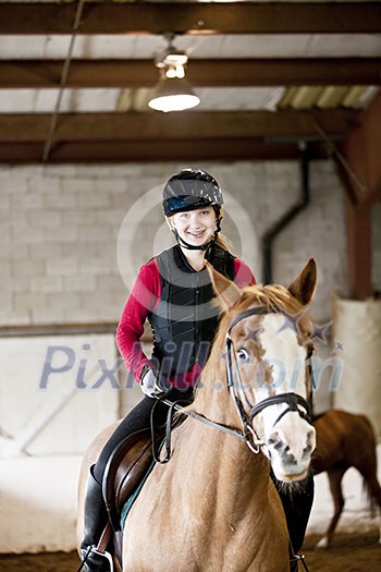 Teenage girl on horseback wearing helmet and safety vest in indoor arena Teenage girl on horseback wearing helmet and safety vest in indoor arena