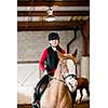 Teenage girl on horseback wearing helmet and safety vest in indoor arena