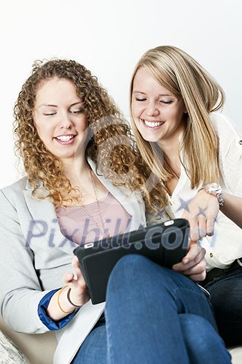 Two young smiling women using tablet computer at home Two young smiling women using tablet computer at home