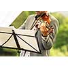 Male violinist playing his instrument and reading a music sheet during an outdoor summer wedding ceremony (shallow DOF; color toned image)
