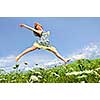 Young teenage girl jumping in summer meadow amid wildflowers