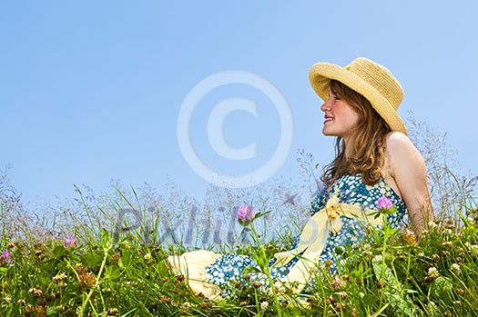 Young teenage girl sitting on summer meadow in straw hat Young teenage girl sitting on summer meadow in straw hat