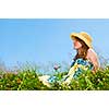 Young teenage girl sitting on summer meadow in straw hat