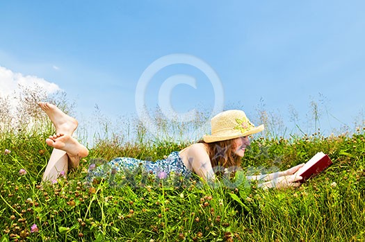 Young teenage girl reading book in summer meadow with straw hat Young teenage girl reading book in summer meadow with straw hat
