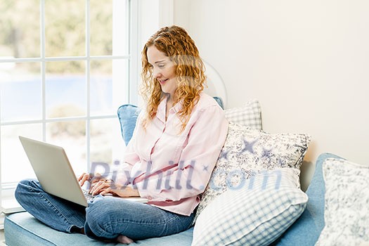 Caucasian woman using laptop computer sitting on couch at home Caucasian woman using laptop computer sitting on couch at home