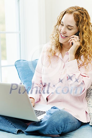 Smiling caucasian woman using laptop computer while on cellphone at home Smiling caucasian woman using laptop computer while on cellphone at home