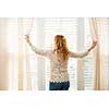 Woman looking out big bright window with curtains and blinds