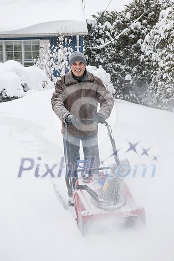 Man using snowblower to clear deep snow on driveway near residential house after heavy snowfall. Man using snowblower to clear deep snow on driveway near residential house after heavy snowfall.