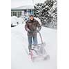 Man using snowblower to clear deep snow on driveway near residential house after heavy snowfall.