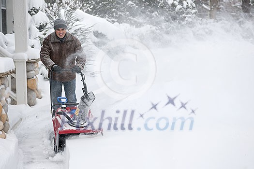 Man using snowblower to clear deep snow on driveway near residential house after heavy snowfall. Man using snowblower to clear deep snow on driveway near residential house after heavy snowfall.