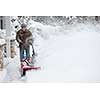 Man using snowblower to clear deep snow on driveway near residential house after heavy snowfall.