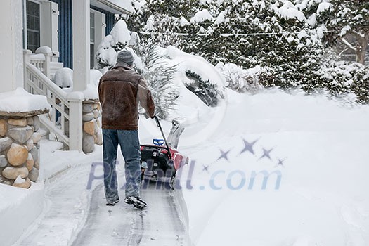 Man using snowblower to clear deep snow on driveway near residential house after heavy snowfall Man using snowblower to clear deep snow on driveway near residential house after heavy snowfall