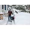 Man using snowblower to clear deep snow on driveway near residential house after heavy snowfall